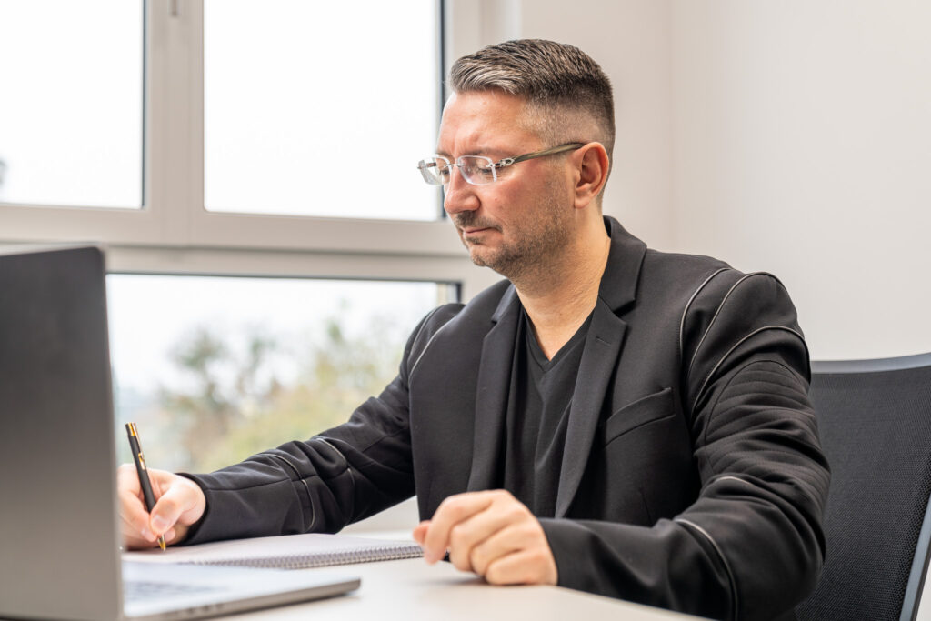 Walter Temmer sitzt am Schreibtisch und hält Kugelschreiber in der Hand