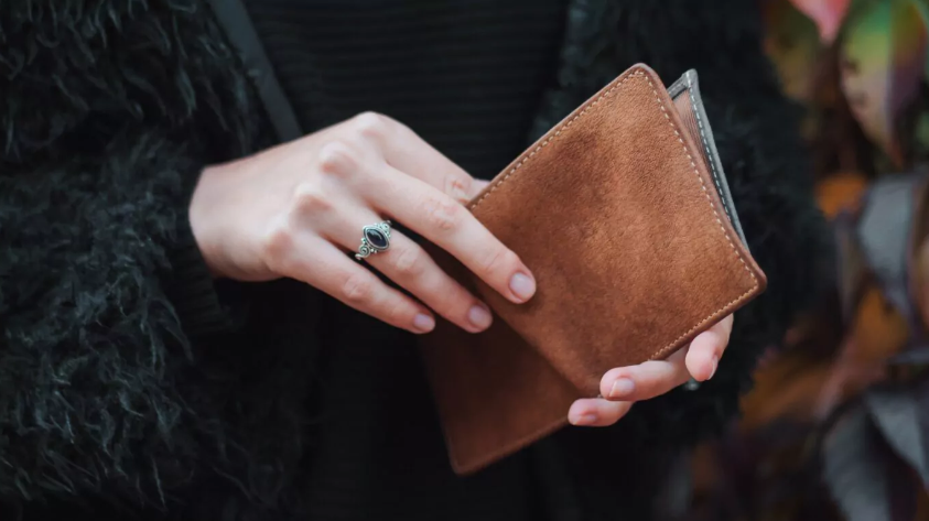 Hand einer Frau hält eine Geldtasche aus braunem Leder die leicht geöffnet ist