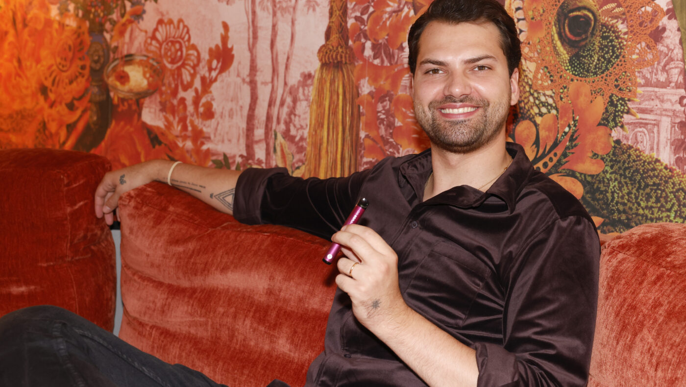 Jimi Blue Ochsenknecht hält E-Zigarette in der Hand und lächelt auf einer Couch sitzend in die Kamera