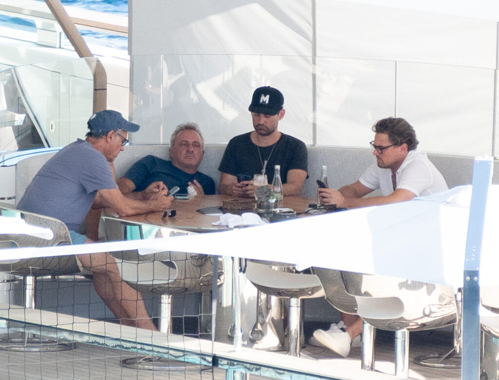 Leonardo DiCaprio sitzt im legeren weißen Hemd mit Freunden an einem Tisch auf der Luxusyacht in Ibiza. 