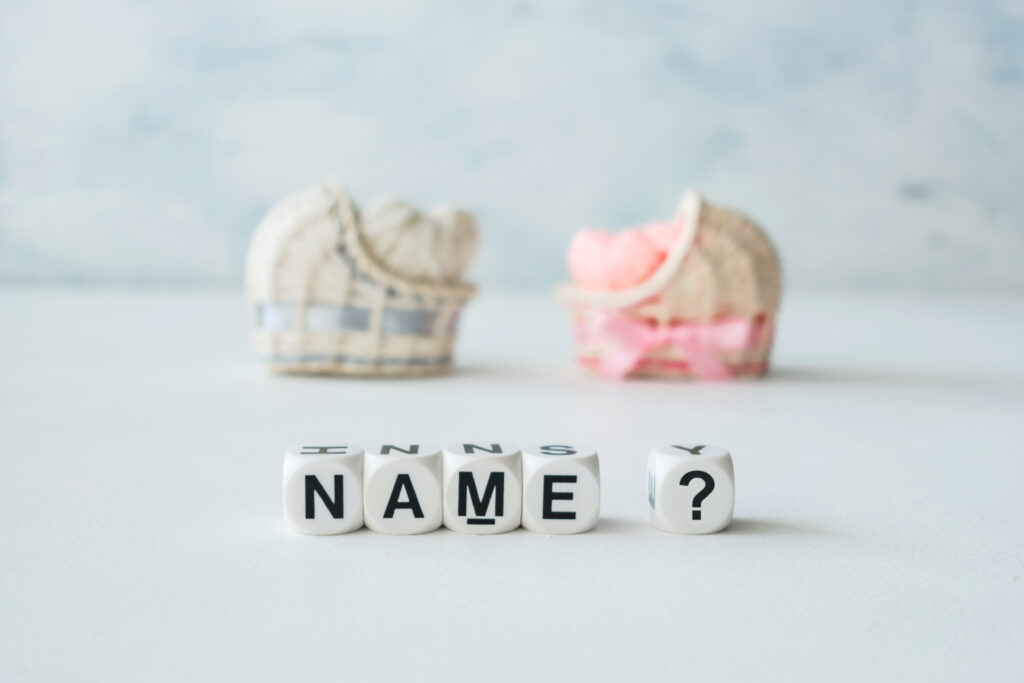 Buchstaben mit Name und Fragezeichen. Dahinter ein blaues und rosarotes Babykörbchen