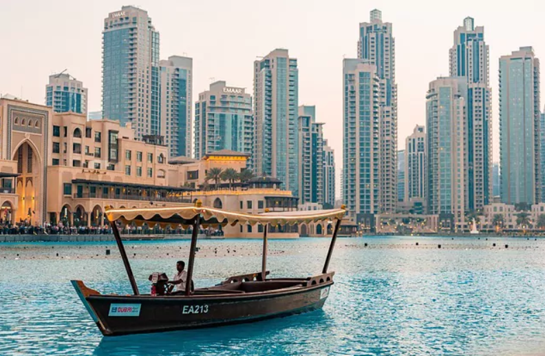 ein kleines Boot aus Holz fährt in Richtung Kamera. Dahinter die Skyline von Wolkenkratzern in Dubai