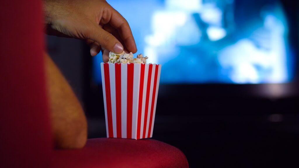 Mann sitzt im Kino und greift in Popcorntüte