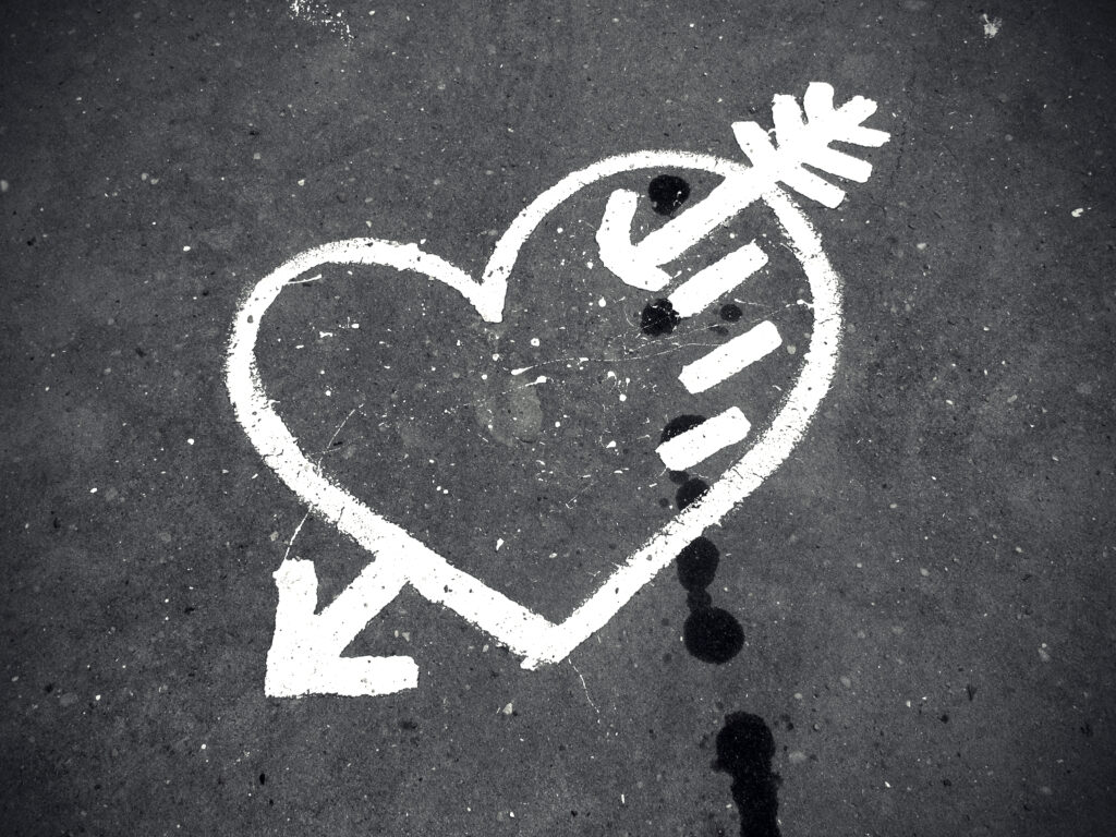 grauer Hintergrund mit einem weißen Herz durch den ein Pfeil geht sowie drei kleine Striche auf der rechten Seite des Herzens