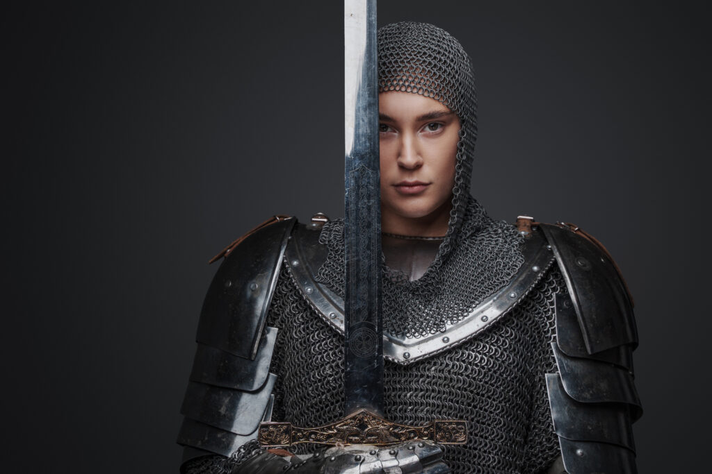 Junges Mädchen in einer Ritterrüstung hält ein Schwert vor ihr Gesicht