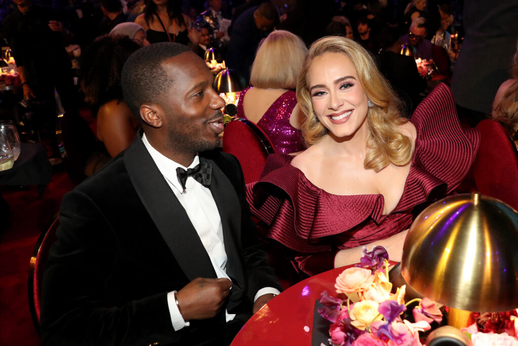 Adele in weinrotem Kleid sitzt bei einer Feier neben Rich Paul der einen schwarzen Anzug trägt