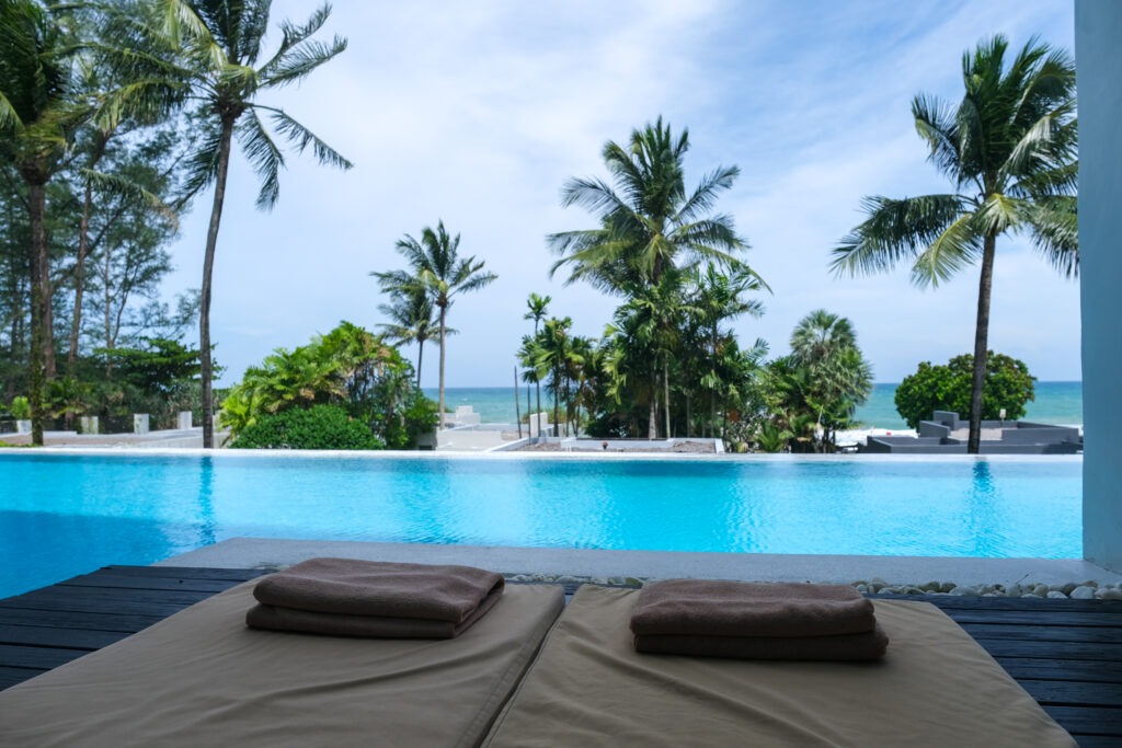 Infinity-Pool vor Palmen und davor zwei braune Strandbetten mit zwei Handtüchern darauf