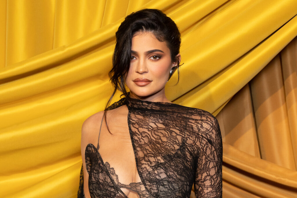 Kylie Jenner mit schwarzem durchsichtigen Kleid vor einem gelben Hintergrund