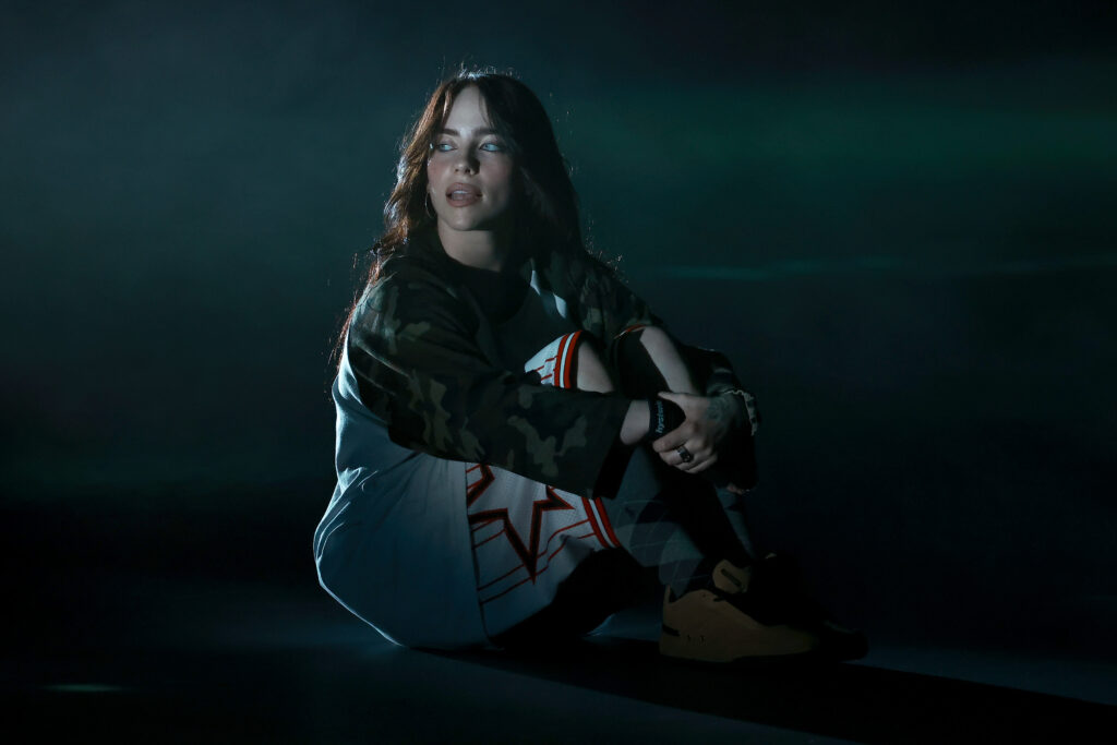 Billie Eilish sitz am Boden und hält sich mit den Händen die Beine