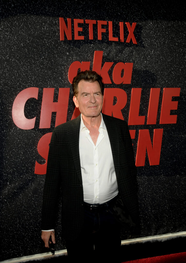 Charlie Sheen posiert vor Netflix-Werbewand in schwarzem Anzug